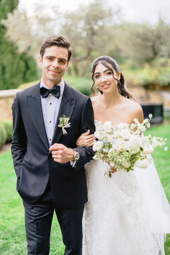 Un couple élégant se tient dans un jardin verdoyant, illustrant une cérémonie de mariage romantique en Provence. 'By Mademoiselle C' transforme ce lieu en un domaine privé pour un grand événement sur mesure. Avec des détails raffinés, cette célébration unique promet une expérience de mariage de luxe, créant des souvenirs inoubliables dans un cadre idyllique.