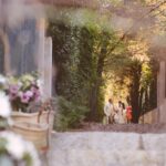 Une élégante cérémonie de mariage dans un domaine privé en Provence, où le couple, entouré de leurs proches, s'avance le long d'un chemin romantique, bordé de fleurs délicates. Cette image évoque une célébration grandiose et sur mesure, mettant en avant l'expertise de 'By Mademoiselle C' en tant que planificateur de mariage de luxe dans la Côte d'Azur et en Corse. L'atmosphère raffinée et sophistiquée, au