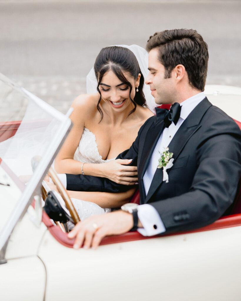 Un couple élégant dans une voiture vintage, célébrant leur rêve de mariage dans un cadre romantique. By Mademoiselle C, expert en organisation de mariages de luxe en Provence, Côte d'Azur et Corse, crée des événements sur mesure. Cette image capture l'essence d'une cérémonie grandiose, entourée de paysages pittoresques, idéale pour une célébration unique et mémorable.