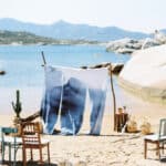 Célébrez votre rêve de mariage avec 'By Mademoiselle C', votre planificateur de mariage de luxe en Provence, Côte d'Azur et Corse. Cette scène idyllique au bord de l'eau met en avant un cadre romantique et élégant, parfait pour une cérémonie grandiose. Les chaises en bois, disposées avec soin sur le sable, créent une atmosphère chaleureuse pour une célébration unique. Le décor minimaliste et naturel, avec les montagnes en arrière