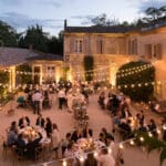 Un élégant dîner en plein air dans un domaine privé, illuminé par des guirlandes lumineuses, créant une atmosphère romantique pour une célébration de luxe. Cette soirée, organisée par By Mademoiselle C, incarne le raffinement d'un mariage sur mesure en Provence, Côte d'Azur et Corse. Les invités savourent un repas exquis dans un cadre sophistiqué, entourés de la beauté des jardins et des bâtiments en pierre. Ce moment unique est le reflet