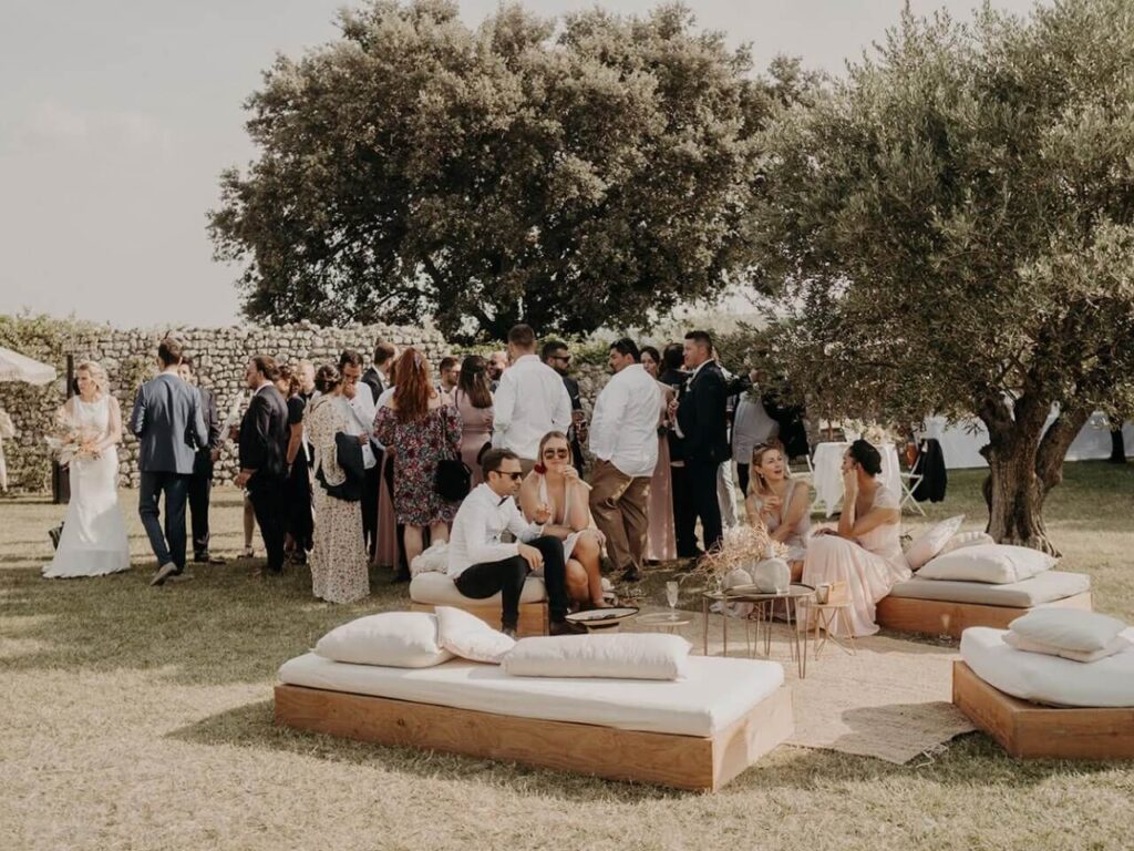 Un mariage romantique et élégant en Provence, avec des invités profitant d'une célébration grandiose dans un domaine privé. Cette scène évoque l'atmosphère d'une cérémonie exceptionnelle, où chaque détail est soigneusement organisé par By Mademoiselle C, le spécialiste des mariages sur mesure. Les convives se détendent sur des canapés en bois, entourés d'un cadre naturel magnifique, parfait pour un événement unique. Ce lieu enchanteur, au cœur des vignob