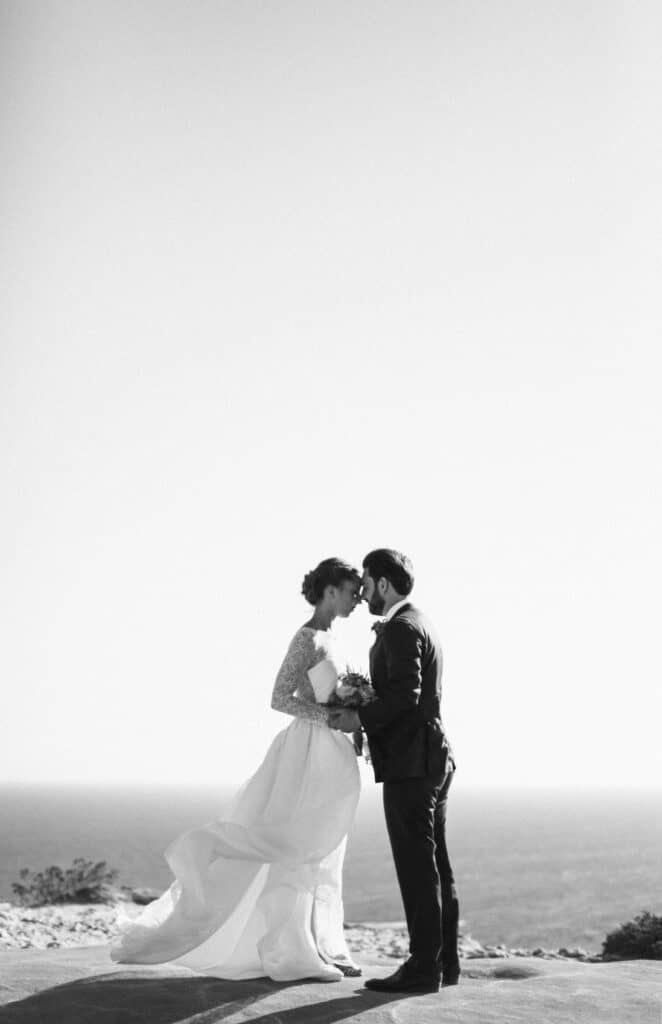 Un couple élégant se tient au sommet d'une falaise, surplombant la mer Méditerranée, incarnant le rêve d'un mariage romantique. Cette image évoque l'atmosphère sophistiquée d'une cérémonie grandiose, parfaitement orchestrée par By Mademoiselle C. Leurs services de planification de mariage sur mesure en Provence, Côte d'Azur et Corse transforment chaque événement en une célébration unique. Les paysages naturels, tels que les montagnes et