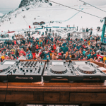 Une ambiance festive et dynamique au cœur des montagnes, où des milliers de personnes se rassemblent pour célébrer un événement unique. L'image montre des équipements de DJ sur une table en bois, avec une foule colorée en arrière-plan, évoquant une atmosphère de grand événement. Bien que cela ne soit pas une scène de mariage, l'énergie et l'excitation rappellent le caractère exceptionnel des célébrations. Pour une expérience de mariage de luxe en Provence, Côte d'Azur et Corse,