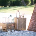 Un élégant coin de réception pour un mariage romantique, mettant en valeur la sophistication d'un événement sur mesure. Les lanternes en verre et les éléments en bois créent une atmosphère chaleureuse, parfaite pour une célébration grandiose dans un domaine privé en Provence. Ce cadre idyllique, entouré de verdure, est idéal pour une cérémonie luxueuse, offrant des lieux exceptionnels pour un rêve de mariage inoubliable. 'By Mademoiselle C' excelle dans l'organisation