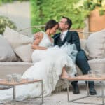 Un couple élégant se détend sur un canapé dans un cadre romantique, illustrant une cérémonie de mariage de luxe organisée par By Mademoiselle C. Cette image évoque une célébration grandiose dans un domaine privé en Provence, où chaque détail est soigneusement orchestré pour créer un événement sur mesure. L'atmosphère sophistiquée, entourée de verdure, souligne la beauté d'un mariage sur-mesure, parfait pour un rêve romantique. Les éléments raffinés et