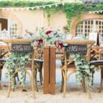 Une décoration élégante et romantique pour un mariage sur mesure dans un domaine privé en Provence, Côte d'Azur et Corse. Les chaises en bois accueillent des pancartes personnalisées "Monsieur" et "Madame", entourées de feuillage luxuriant et de fleurs délicates. Ce cadre idyllique évoque une célébration grandiose, idéale pour un événement unique. Avec des tables soigneusement dressées, cet espace extérieur crée l'atmosphère parfaite pour un mariage de