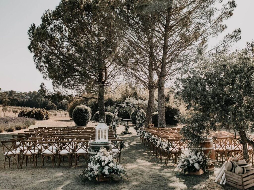 Un cadre romantique et élégant pour une cérémonie de mariage sur mesure, mettant en avant des chaises en bois disposées sous des arbres majestueux. Ce lieu exceptionnel, niché dans un domaine privé en Provence, évoque une atmosphère de luxe et de sophistication, parfaite pour une grande célébration. Les touches florales délicates ajoutent une note de charme à cet événement unique, idéal pour un rêve de mariage dans un cadre idyllique. By Mademoiselle C transforme chaque instant en