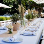 Table élégamment dressée pour une célébration romantique en plein air, mettant en avant le savoir-faire de By Mademoiselle C en tant que Wedding Planner en Provence, Côte d'Azur & Corsica. Les éléments naturels tels que des plantes vertes et des fleurs délicates créent une atmosphère sophistiquée pour un grand événement. La disposition soigneusement pensée reflète une organisation sur mesure, idéale pour un mariage de luxe ou une cérémonie grandiose dans un domaine privé. Ce