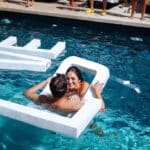 Un couple joyeux s'embrasse dans une piscine luxueuse, entouré d'une atmosphère romantique et élégante, illustrant parfaitement le savoir-faire de By Mademoiselle C en matière de planification de mariage. Ce moment unique évoque une célébration grandiose, idéale pour un mariage sur mesure en Provence, Côte d'Azur et Corse. Avec des éléments de design raffinés et des lieux d'exception, cette scène capture l'essence d'une cérémonie de rêve,