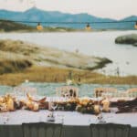 Une somptueuse table de réception pour un mariage romantique au bord de la mer, organisée par By Mademoiselle C, wedding planner de luxe en Provence, Côte d'Azur et Corse. Cette scène idyllique met en avant un cadre élégant avec des bougies scintillantes et des fleurs délicates, créant une atmosphère intime pour une célébration unique. Le décor naturel, entouré de montagnes et de rochers, souligne le caractère exceptionnel de ce domaine privé, parfait pour