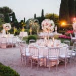 Une élégante réception de mariage en plein air dans un jardin luxuriant, mettant en valeur la beauté des lieux d'exception en Provence, Côte d'Azur et Corse. Les tables, soigneusement dressées pour un grand événement, sont ornées de superbes compositions florales, créant une atmosphère romantique et sophistiquée. Ce cadre idéal pour une célébration grandiose est parfaitement organisé par By Mademoiselle C, spécialiste des mariages sur mesure. Chaque détail reflète