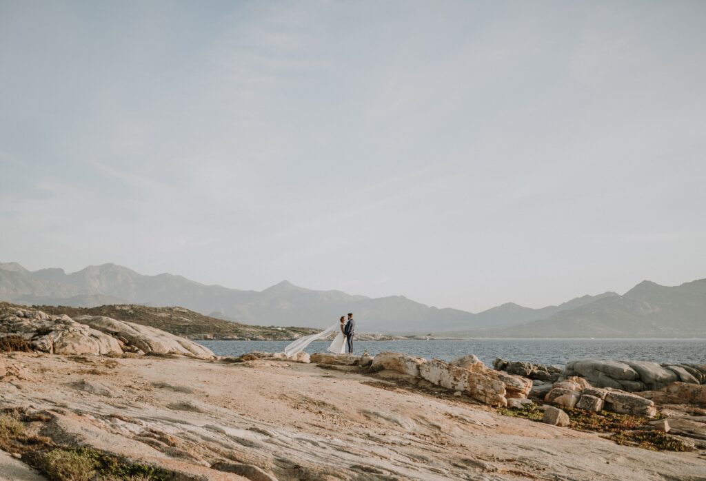 Un couple s'échange des vœux sur une plage isolée en Corse, entouré par des montagnes majestueuses et une mer scintillante. Cette scène évoque un mariage romantique et luxueux, parfaitement organisé par By Mademoiselle C. Offrant des lieux exceptionnels pour une célébration sur mesure, chaque détail contribue à créer un événement unique et mémorable.