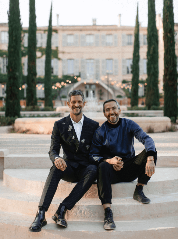 Un couple élégant souriant sur les marches d'un domaine privé en Provence, illustrant l'expertise de By Mademoiselle C en tant que wedding planner de luxe. Ce cadre romantique et sophistiqué est idéal pour une cérémonie grandiose ou un mariage sur mesure, entouré de paysages enchanteurs et de lieux d'exception. Créez votre rêve de célébration unique dans la Côte d'Azur et en Corse.