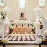 Une élégante cérémonie de mariage se déroule dans une chapelle, décorée de somptueuses fleurs blanches et de bougies, créant une atmosphère romantique et sophistiquée. En tant que Wedding Planner en Provence, Côte d'Azur & Corsica, By Mademoiselle C organise des événements de luxe sur mesure, transformant chaque moment en une célébration grandiose. Ce cadre exceptionnel, avec ses détails raffinés, illustre parfaitement une expérience de mariage unique,