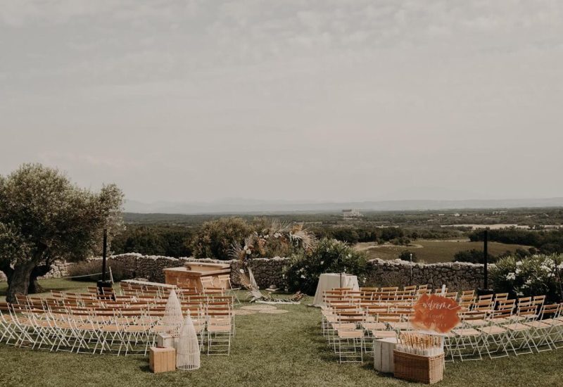 Cérémonie romantique en plein air dans un domaine privé en Provence, Côte d'Azur et Corse, organisée par By Mademoiselle C. Cette scène élégante, entourée de paysages verdoyants et de montagnes, illustre parfaitement un mariage de luxe sur mesure. Les chaises en bois disposées avec soin offrent une atmosphère intime pour une célébration grandiose. Un cadre exceptionnel pour un événement unique, où chaque détail est pensé pour créer le mariage de vos rêves.