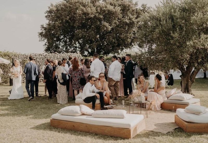 Un mariage romantique et luxueux en Provence, avec des invités profitant d'un cadre élégant sous des arbres centenaires. Cette célébration sur un domaine privé met en valeur une organisation sur mesure, idéale pour un événement unique. Les canapés en bois et les coussins créent une atmosphère conviviale pour un moment de partage durant cette cérémonie grandiose. Parfait pour un rêve de mariage dans un environnement enchanteur, ce lieu exceptionnel incarne l'expertise de By M