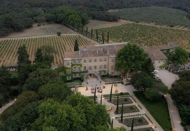 Une vue aérienne d'un élégant domaine privé entouré de vignobles, parfait pour un mariage de luxe en Provence. Ce lieu exceptionnel est idéal pour une cérémonie romantique et une célébration grandiose, offrant une atmosphère sophistiquée pour un événement sur mesure. Les jardins soigneusement entretenus et les bâtiments historiques créent le cadre parfait pour un rêve de mariage, où chaque détail est organisé avec soin par By Mademoiselle C, spécialiste des mariages uniques sur la Côte d