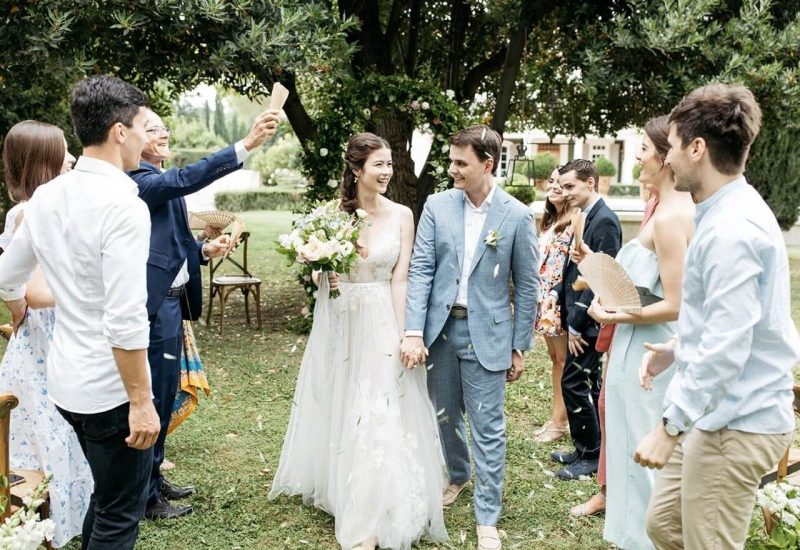 Un couple rayonnant célèbre leur mariage dans un jardin élégant, entouré de leurs proches, illustrant parfaitement une célébration romantique et unique. Cet événement sur mesure, organisé par By Mademoiselle C, incarne le luxe d'un mariage en Provence, avec des éléments de nature verdoyante et une ambiance sophistiquée. La cérémonie grandiose se déroule dans un domaine privé, offrant un cadre exceptionnel pour un mariage de rêve. Les invités, joyeux et accueillants, ajout