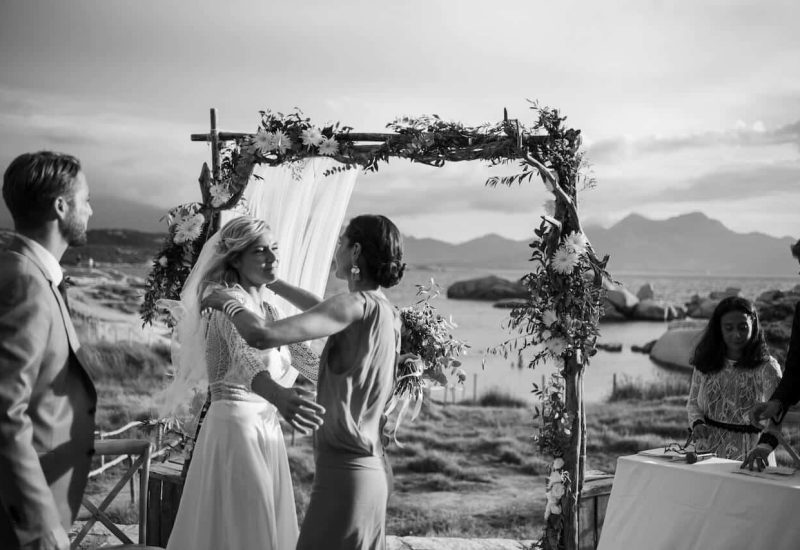 Célébration romantique au bord de l'eau avec un cadre époustouflant, mettant en avant les compétences de 'By Mademoiselle C', votre wedding planner en Provence, Côte d'Azur et Corse. Cette cérémonie de luxe, entourée de paysages magnifiques et de montagnes, illustre parfaitement un mariage sur mesure dans un domaine privé. La scène évoque une atmosphère élégante et sophistiquée, idéale pour une grande célébration ou un événement unique. Chaque détail est