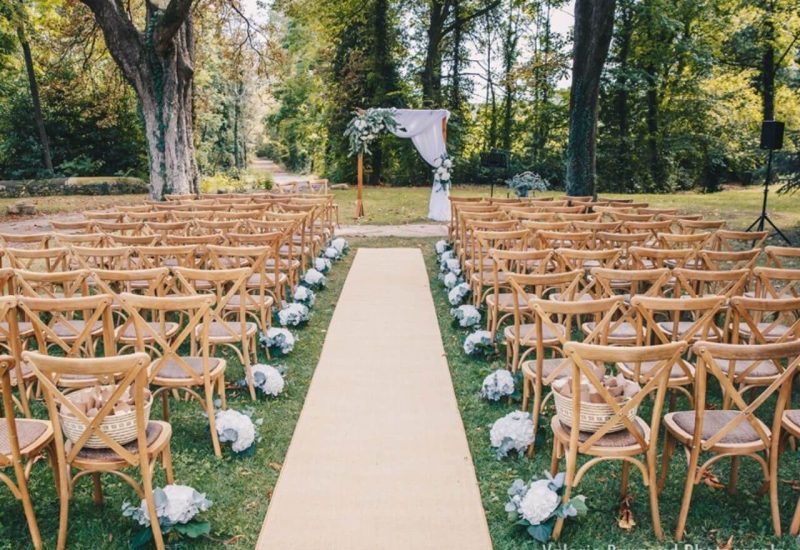 Cérémonie de mariage romantique en plein air, organisée par By Mademoiselle C, mettant en valeur un cadre élégant et naturel. Les chaises en bois délicatement disposées entourent un allée de tapis, créant une atmosphère sophistiquée pour un grand événement. Idéal pour un mariage sur mesure dans un domaine privé, ce lieu exceptionnel en Provence offre le cadre parfait pour une célébration grandiose. Les fleurs blanches ajoutent une touche de charme à cette