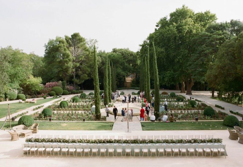 Un cadre romantique et élégant pour un mariage de luxe à Provence, Côte d'Azur et Corse. Ce jardin exquis, avec ses allées bordées de cyprès et ses parterres de fleurs soigneusement entretenus, est l'endroit idéal pour une cérémonie grandiose. La disposition sur mesure des chaises témoigne de l'organisation bespoke de 'By Mademoiselle C', créant une atmosphère sophistiquée pour une célébration unique. Ce lieu exceptionnel, entouré de