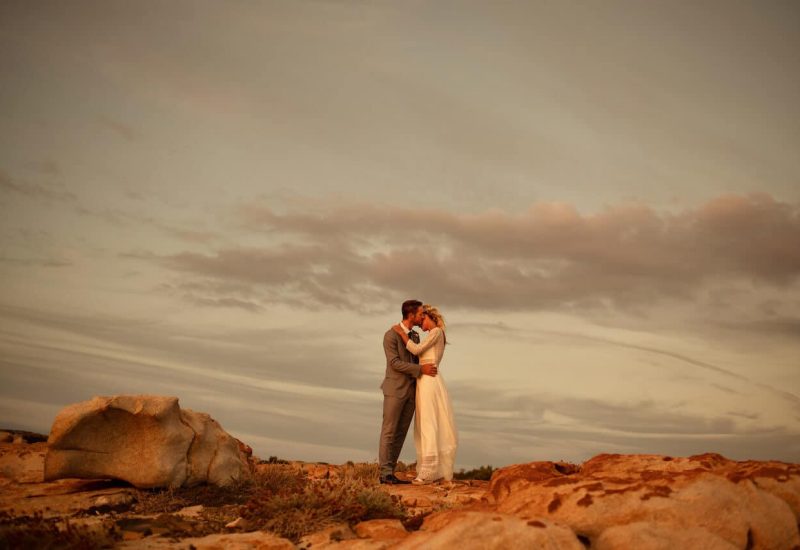 Couple amoureux s'embrassant sur une plage de Provence, créant une ambiance romantique et élégante. Cette cérémonie de mariage de luxe, organisée par By Mademoiselle C, incarne l'essence d'un événement sur mesure dans des lieux exceptionnels. Le cadre naturel, avec ses rochers et son ciel doré, évoque une célébration grandiose, parfaite pour un mariage de rêve en Côte d'Azur. Chaque détail est soigneusement pensé pour offrir une expérience