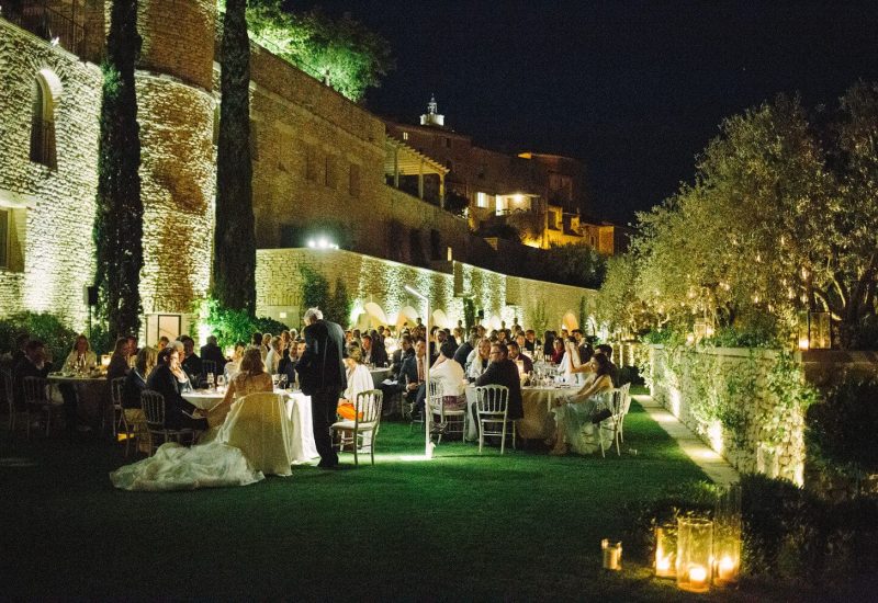 Une magnifique réception de mariage en plein air, organisée par By Mademoiselle C, se déroule dans un domaine privé en Provence. Les invités, entourés de lumières tamisées et d'une atmosphère romantique, profitent d'un grand banquet sous les étoiles. Ce luxe mariage, avec ses tables élégamment dressées, souligne la sophistication d'une célébration sur mesure. Le cadre enchanteur, agrémenté de jardins luxuriants et de pierres anciennes, en fait un lieu idéal