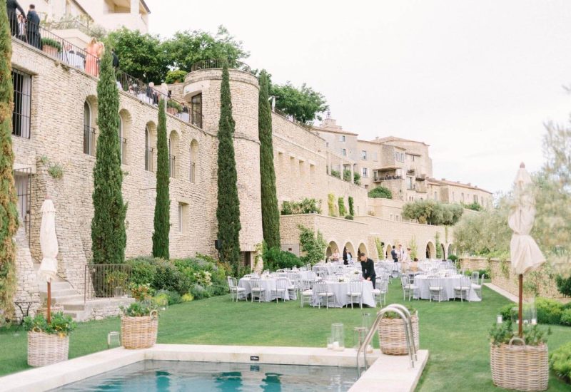 Un cadre élégant pour une célébration de mariage dans un domaine privé en Provence, où la beauté des paysages se marie à une atmosphère romantique. Cette image illustre un grand événement sur une pelouse verdoyante, entourée de cyprès majestueux et de pierres dorées, idéale pour un mariage de luxe. Les tables soigneusement dressées reflètent l'expertise de By Mademoiselle C dans l'organisation de cérémonies sur mesure. Un lieu d'exception pour un