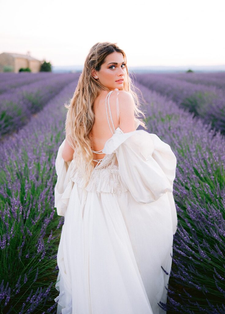 Dans un champ de lavande en Provence, une mariée rayonnante se tourne avec élégance, incarnant le rêve d'une cérémonie romantique. 'By Mademoiselle C' excelle dans l'organisation de mariages de luxe et sur mesure, créant des événements uniques dans des lieux exceptionnels. Offrant une célébration grandiose, chaque détail reflète la sophistication des mariages en Côte d'Azur et en Corse.