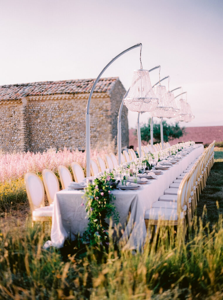 Une élégante table de réception, ornée de délicates fleurs, se dresse dans un champ de lavande, évoquant une ambiance romantique pour un mariage de luxe. Ce cadre idyllique, situé dans un domaine privé en Provence, offre un cadre unique pour une célébration grandiose. Avec des éléments sur mesure, 'By Mademoiselle C' réalise des événements exceptionnels, créant des souvenirs inoubliables pour chaque couple.