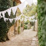 Un chemin romantique bordé de pierres anciennes et de verdure luxuriante, idéal pour une cérémonie de mariage grandiose en Provence. L'atmosphère élégante et sophistiquée de cet espace privé met en valeur l'organisation sur mesure d'un événement unique, parfait pour un mariage de luxe. Les guirlandes délicates ajoutent une touche de charme à cette célébration exceptionnelle, faisant de cet endroit un cadre rêvé pour un mariage sur mesure dans la Côte d'Azur et