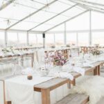 Une élégante salle de réception sous un chapiteau transparent, mettant en valeur une décoration raffinée pour une cérémonie romantique. Les tables en bois, soigneusement dressées, accueillent des fleurs délicates et des bougies, créant une atmosphère chaleureuse pour un grand événement. Ce cadre idyllique, situé dans un domaine privé, est parfait pour une célébration de mariage sur mesure. Avec des vues imprenables sur les vignobles environnants, cet espace incarne le