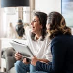 Deux femmes souriantes discutent d'un projet de mariage dans un cadre élégant, mettant en avant le savoir-faire de By Mademoiselle C, wedding planner en Provence, Côte d'Azur et Corse. L'atmosphère romantique et sophistiquée de cet échange évoque la création d'une cérémonie grandiose dans un domaine privé. Avec une approche sur mesure, elles envisagent un mariage de luxe, conçu avec soin pour offrir une expérience unique. Ce moment illustre parfaitement l'eng