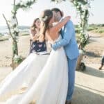 Célébration romantique d'un mariage de luxe sur une plage pittoresque, mettant en avant un couple échangeant un baiser sous un arc floral. L'atmosphère élégante et sophistiquée reflète l'expertise de By Mademoiselle C en tant que planificateur de mariage en Provence, Côte d'Azur et Corse. Cet événement sur mesure, organisé dans un cadre idyllique, évoque un rêve de mariage unique, parfait pour une grande cérémonie. Les