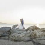 Un couple amoureux se tient sur des rochers au bord de la mer, au coucher du soleil, incarnant l'essence d'un mariage romantique en Provence. Ce moment magique illustre le savoir-faire de By Mademoiselle C en tant que planificateur de mariage de luxe, créant des célébrations sur mesure dans des lieux exceptionnels. Avec l'océan scintillant en arrière-plan, cette scène évoque une cérémonie grandiose, parfaite pour un événement unique dans un domaine privé