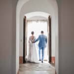 Un couple se tenant par la main, sortant d'une élégante demeure, symbolisant un moment romantique et intime, parfait pour un mariage de luxe en Provence, Côte d'Azur et Corse. Cette scène évoque une organisation sur mesure d'une cérémonie grandiose dans un domaine privé, où chaque détail est pensé pour créer un événement unique. L'atmosphère raffinée et sophistiquée de cet endroit sublime souligne l'expertise de 'By Mademoiselle C' dans la création