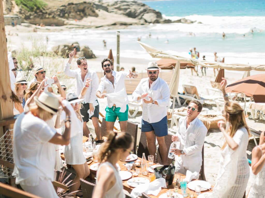 Une célébration luxueuse sur la plage en Provence, Côte d'Azur, mettant en valeur une ambiance romantique et élégante. Ce mariage sur la plage, organisé par By Mademoiselle C, incarne le rêve d'une cérémonie sur mesure, entourée par des amis joyeux. Les invités, habillés en blanc, profitent d'un cadre idyllique, avec des parasols et des chaises longues en arrière-plan, créant une atmosphère de grand événement. Chaque détail