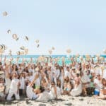 Une célébration de mariage unique sur la plage, mettant en scène un groupe joyeux en tenue estivale, incarnant l’esprit d’un mariage romantique et élégant. Ce grand événement, organisé par By Mademoiselle C, évoque une cérémonie de luxe au bord de l'eau, avec des invités lançant des chapeaux en l'air, symbolisant la joie d'une journée mémorable. Niché dans un cadre exceptionnel de la Côte d'Azur, ce mariage sur la plage