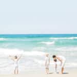 Une mère et ses enfants s'émerveillent sur une plage ensoleillée de la Côte d'Azur, symbolisant l'atmosphère romantique et élégante des événements organisés par By Mademoiselle C. Cette scène évoque des souvenirs de célébrations de luxe et de mariages sur mesure dans des lieux exceptionnels. L'environnement côtier, avec ses vagues scintillantes et son ciel azur, rappelle le cadre parfait pour une cérémonie grandiose ou une célébration